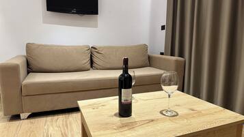 A modern living room with a beige sofa, a wooden coffee table, a bottle of wine, and an empty wine glass.