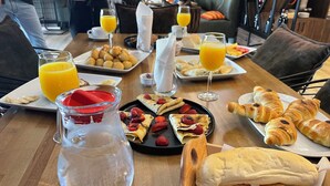 Un desayuno con cruasanes, pastelería y fruta en platos, junto con vasos de jugo de naranja.