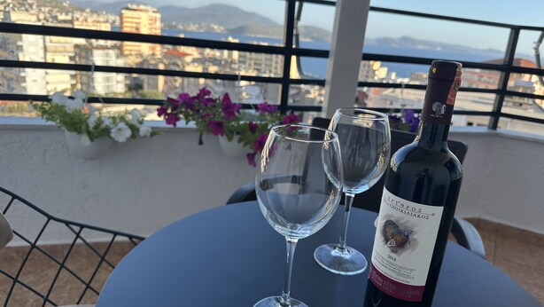 Una mesa con una botella de vino y dos copas en un balcón con vistas a un paisaje urbano.