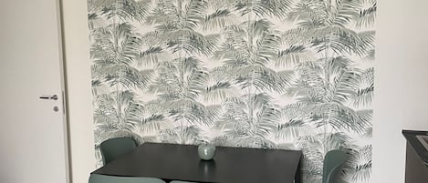 Un comedor con una mesa y cuatro sillas, una manzana pequeña sobre la mesa y una pared con un diseño de hojas.