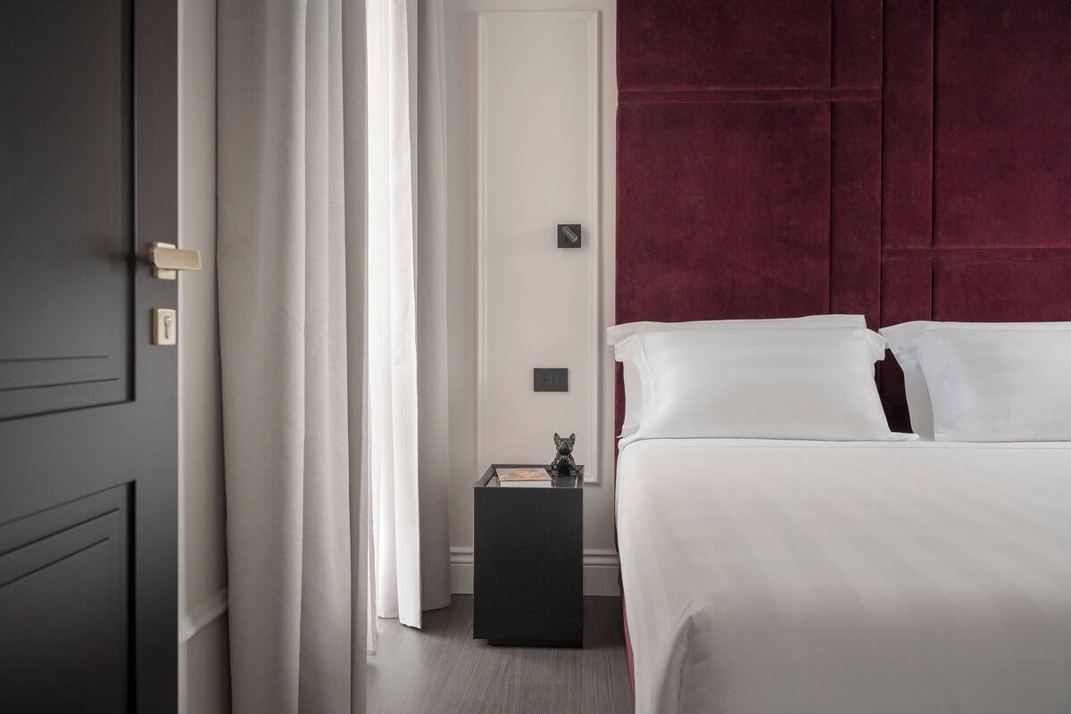 A hotel room with a bed, a nightstand, a door, and a red headboard.