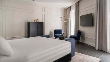 A modern hotel room with a large bed, a desk, two chairs, a TV, and a wardrobe.