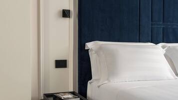 Un dormitorio moderno con un cabecero azul oscuro, ropa de cama blanca y una mesita de noche negra con un libro.