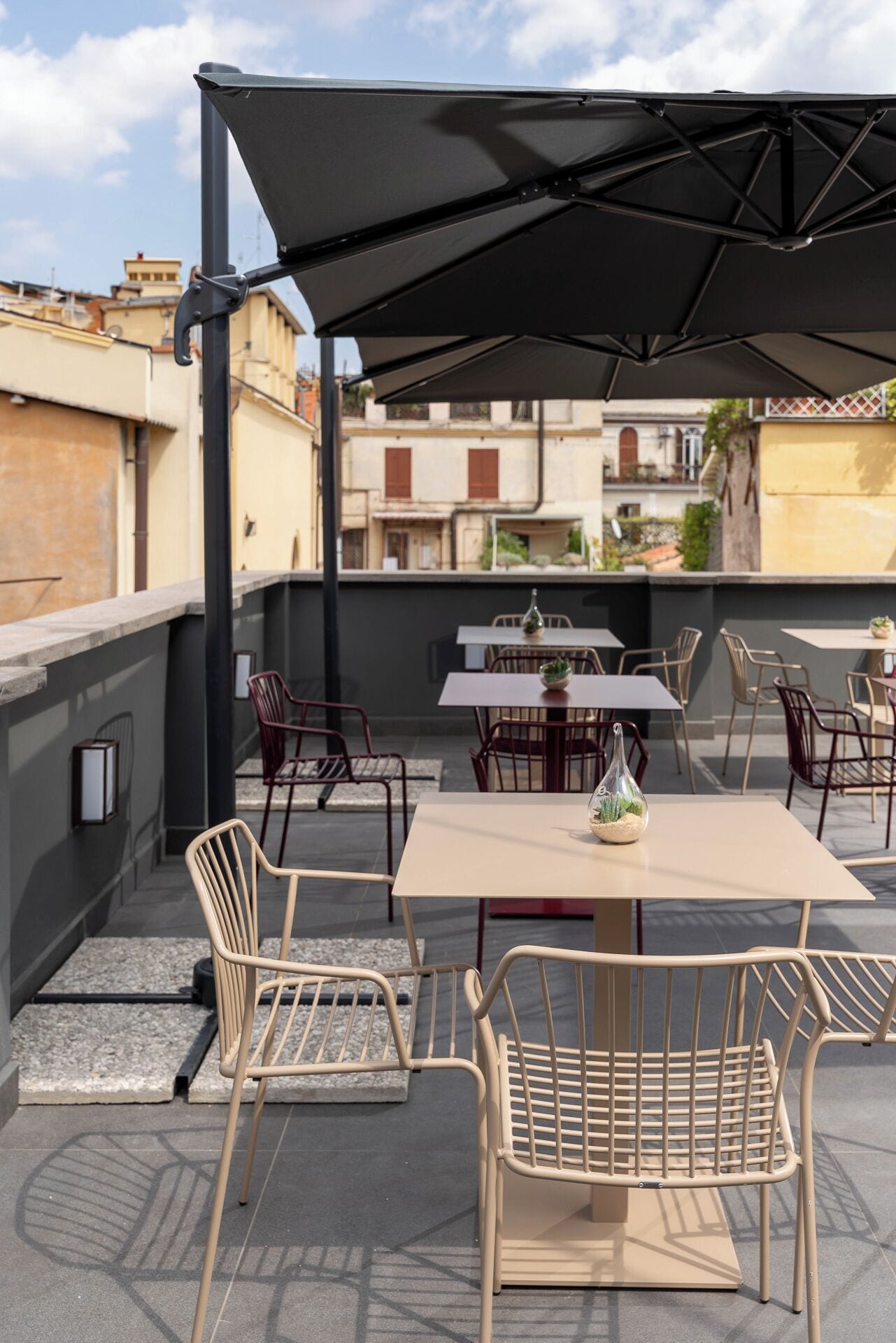 An outdoor patio with tables and chairs, a large umbrella, and a view of buildings in the background.
