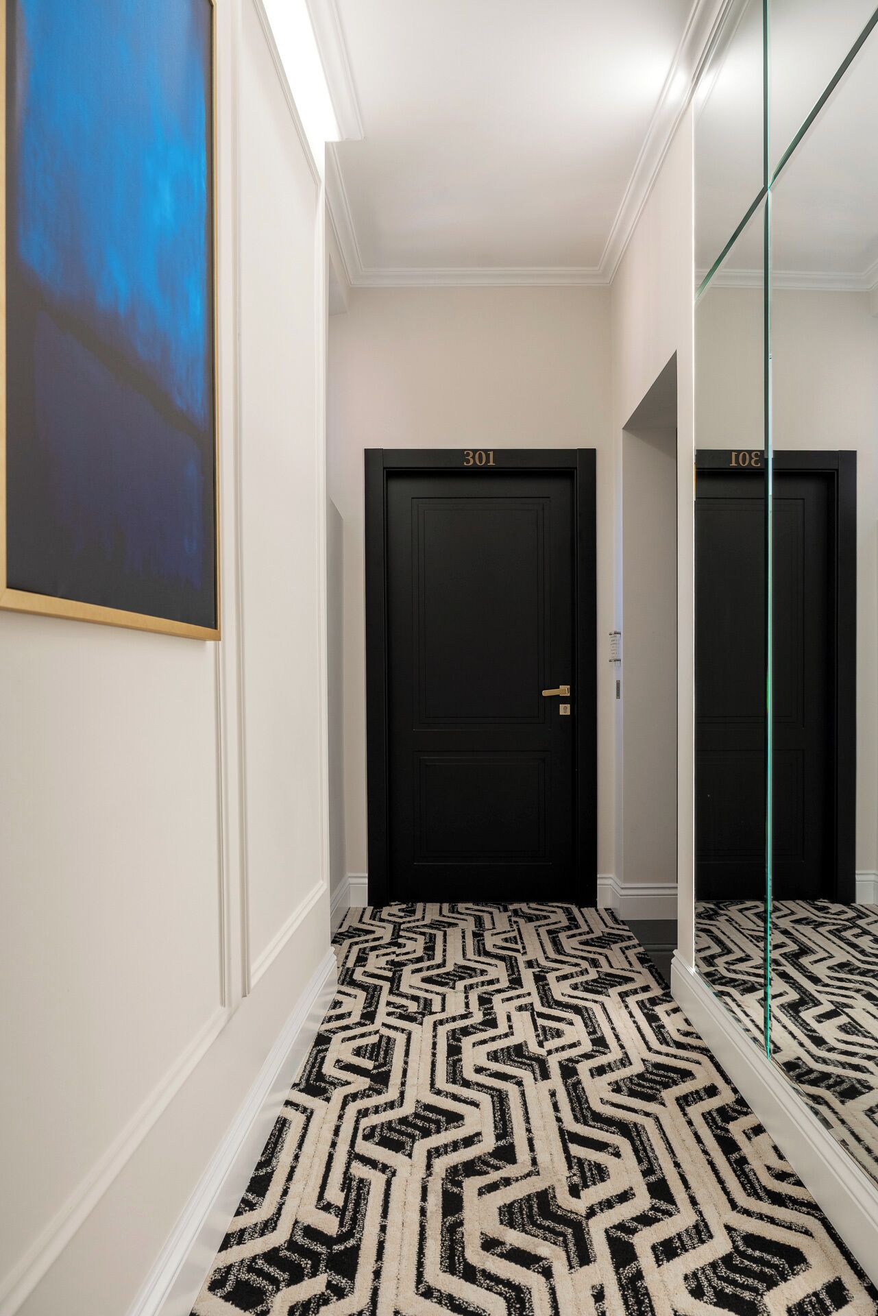 A hallway with a black door labeled "301", a patterned carpet, and a large mirror on the right.
