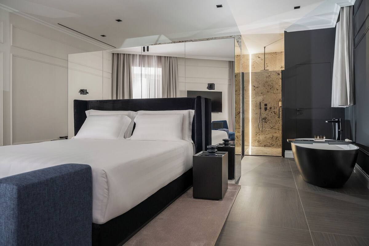A modern hotel room with a large bed, a separate bathroom with a bathtub, and a large mirror.