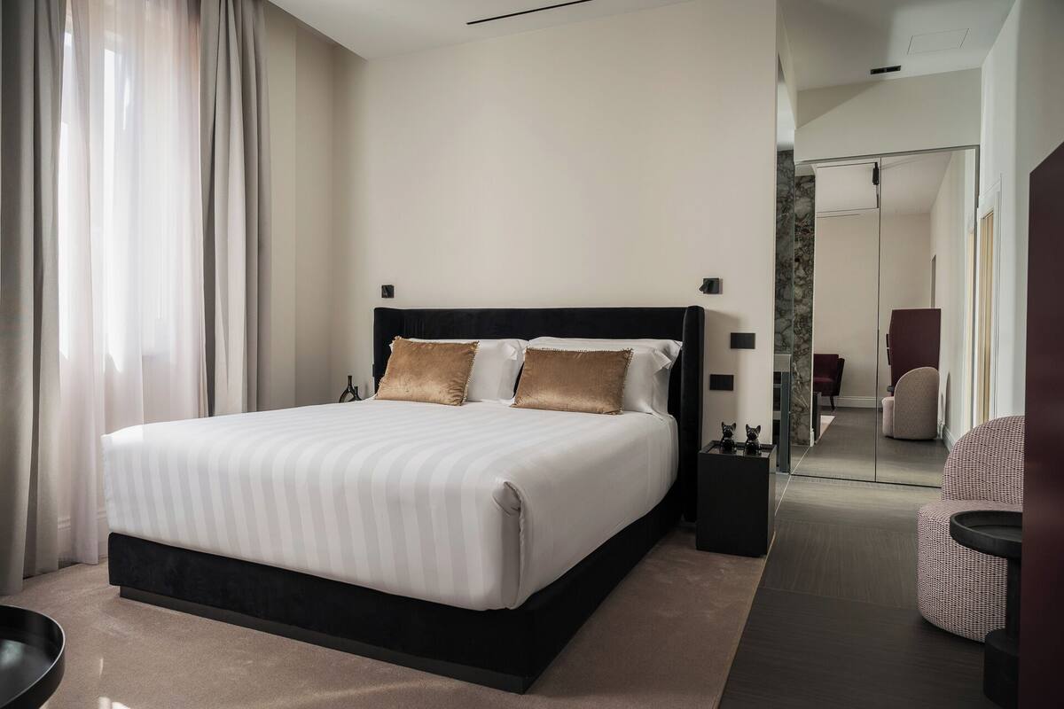 A modern hotel room with a large bed, a bedside table, and a mirror.