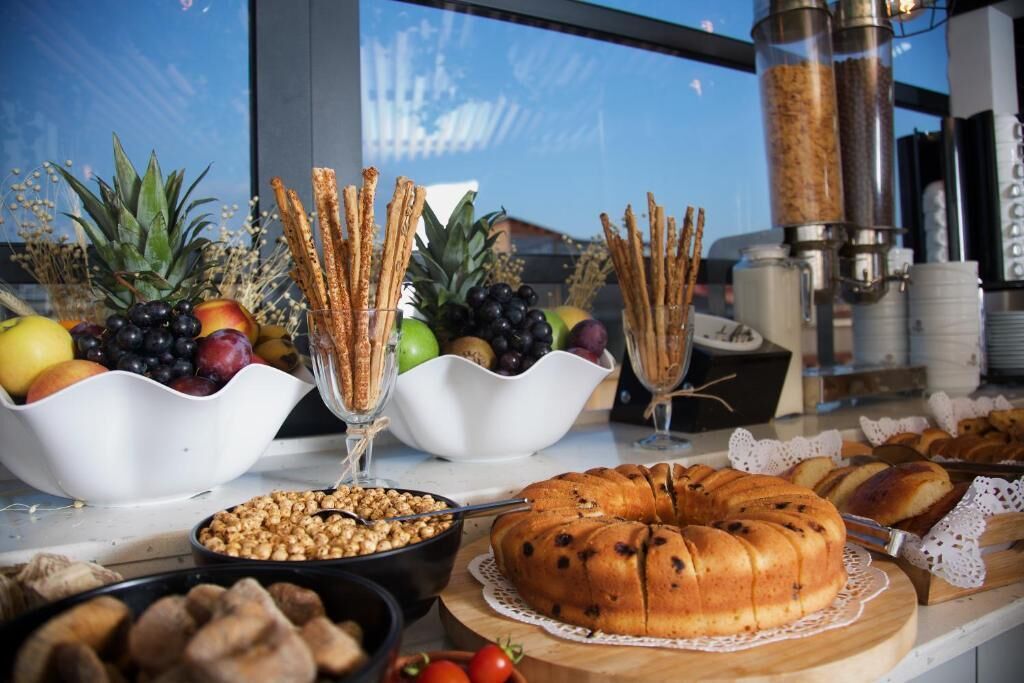 Una mesa de bufé con diversos alimentos, entre ellos frutas, nueces y un pastel bundt, frente a una ventana con vistas.