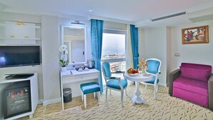 A hotel room with a TV, a desk, a chair, a pink sofa, and a view of the sea. - Glamour Hotel Istanbul Sirkeci (Istanbul)