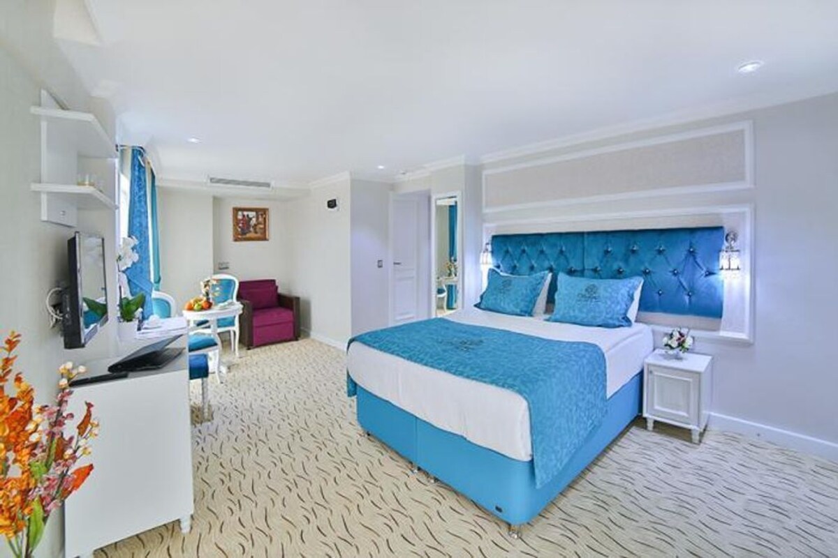 Habitación de hotel con una cama grande, un escritorio con computadora, una silla y una mesita de noche con lámpara.