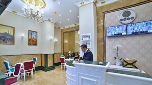 A hotel reception area with a receptionist, a reception desk, a clock, and multiple screens displaying images. - Glamour Hotel Istanbul Sirkeci (Istanbul)
