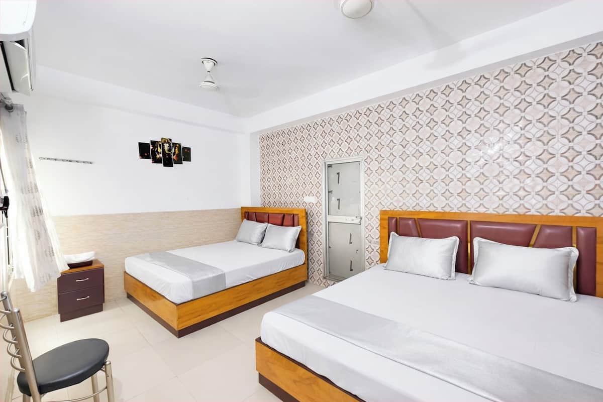 A hotel room with two beds, a desk, a chair, a wardrobe, and a patterned wall.