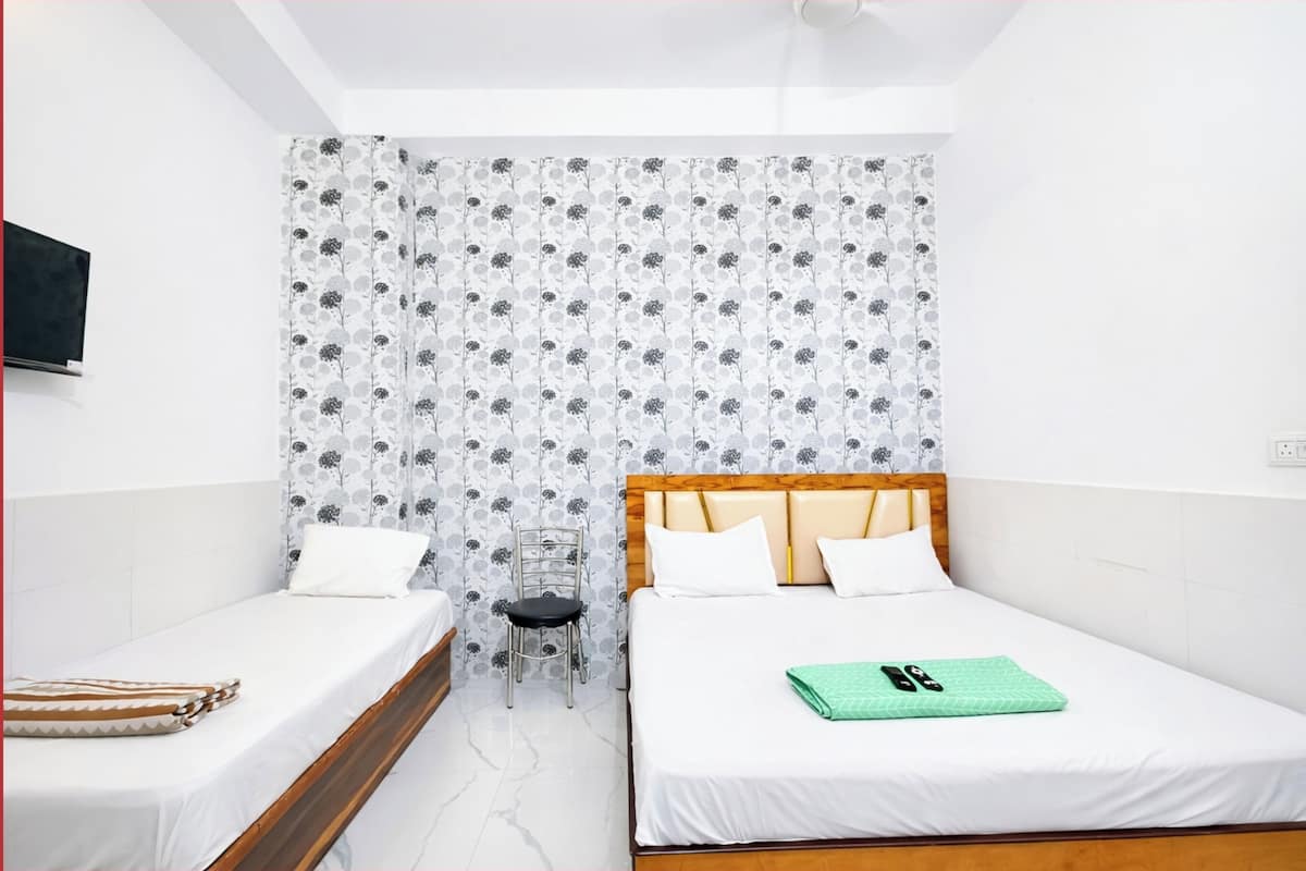 A room with two beds, a chair, a TV, and a patterned wall.