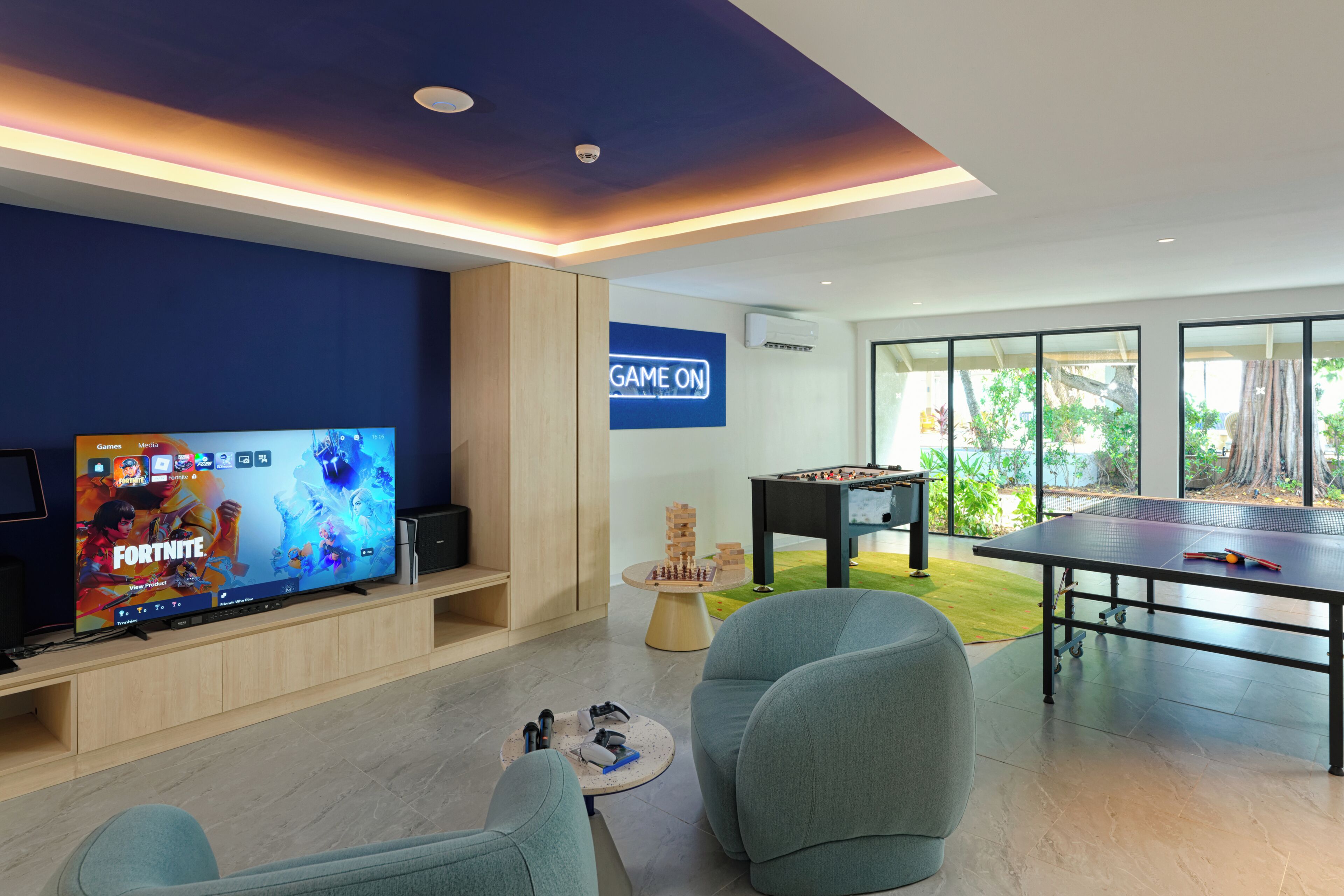 A modern living room with a large flat-screen TV, comfortable seating, a foosball table, and a 'GAME ON' sign.