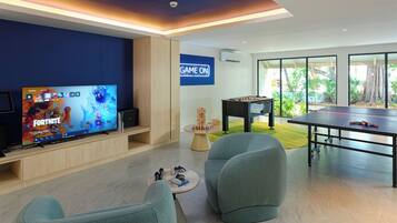 A modern living room with a large flat-screen TV, comfortable seating, a foosball table, and a 'GAME ON' sign.
