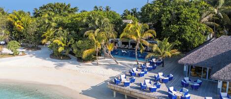 Un resort en la playa con piscina, sillas de descanso y una construcción de techo de paja.