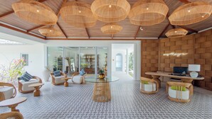 Een ruime kamer met een hoge plafond, zittingen van riet, een glazen tafel en riemeubilair.