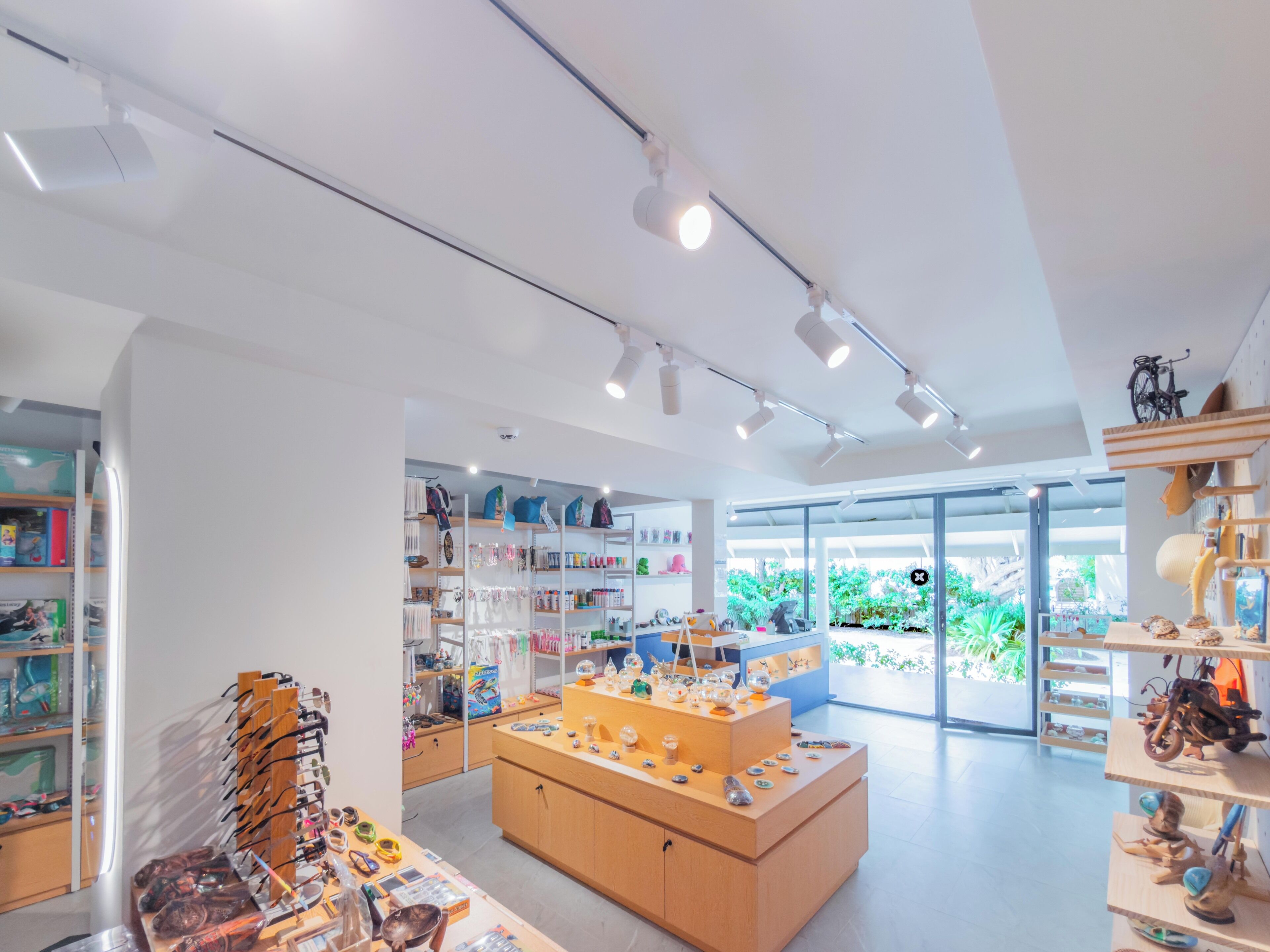 Un espacio comercial moderno con estanterías ordenadas, una mesa de exhibición central y vistas a zonas verdes exteriores.