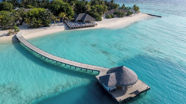 Een overwater bungalow met rieten dak, een houten looppad en uitzicht op het strand.