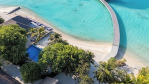 Luchtbeeld van een resort met een zwembad, een terrasgedeelte en bungalows boven het water.
