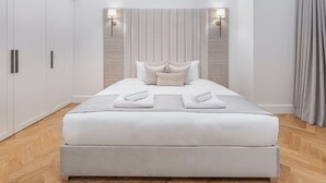 A modern bedroom with a large bed, a wardrobe, and two wall-mounted lights. - Wimpole Mews - 4 Bedroom Apartment (London)