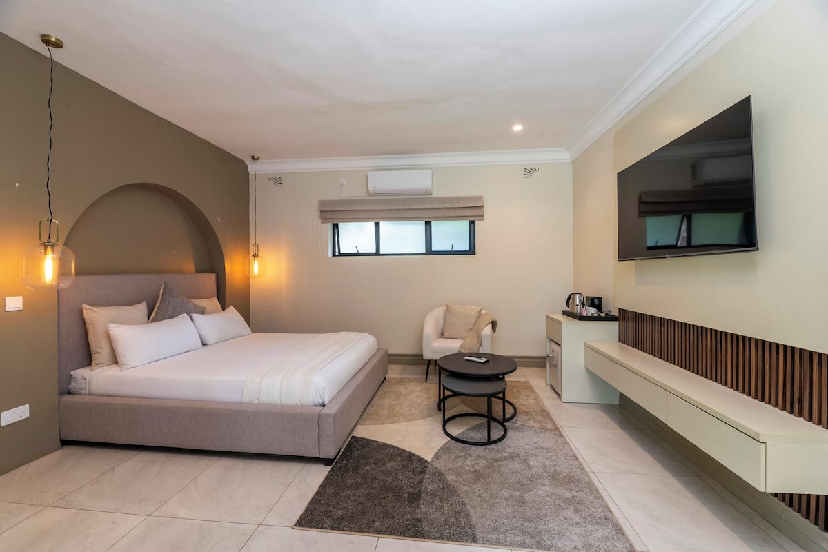 Un dormitorio moderno con cama, mesita de noche, silla, televisor y banco empotrado.