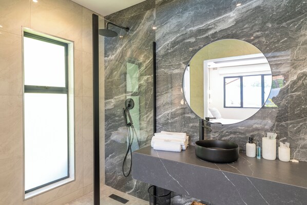 Une salle de bain moderne avec un grand miroir, un lavabo noir et une douche.