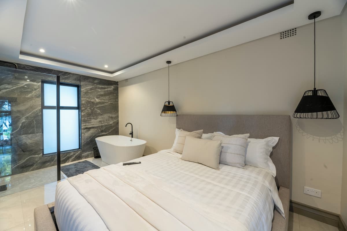 Un dormitorio moderno con una cama grande, una bañera blanca redonda y una zona de ducha con paredes de cristal.