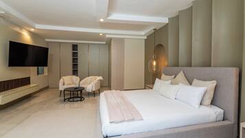 A modern bedroom with a large bed, a flat-screen TV, a seating area with chairs, and a built-in wardrobe.