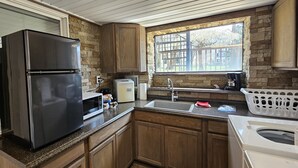 A kitchen with a refrigerator, microwave, sink, and a window with a view of buildings. - Shoreline Estates - Glamping B (Confluence)