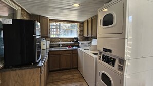A compact kitchen with wooden cabinets, a black refrigerator, a sink, and stacked appliances including a washer and dryer. - Shoreline Estates - Glamping B (Confluence)