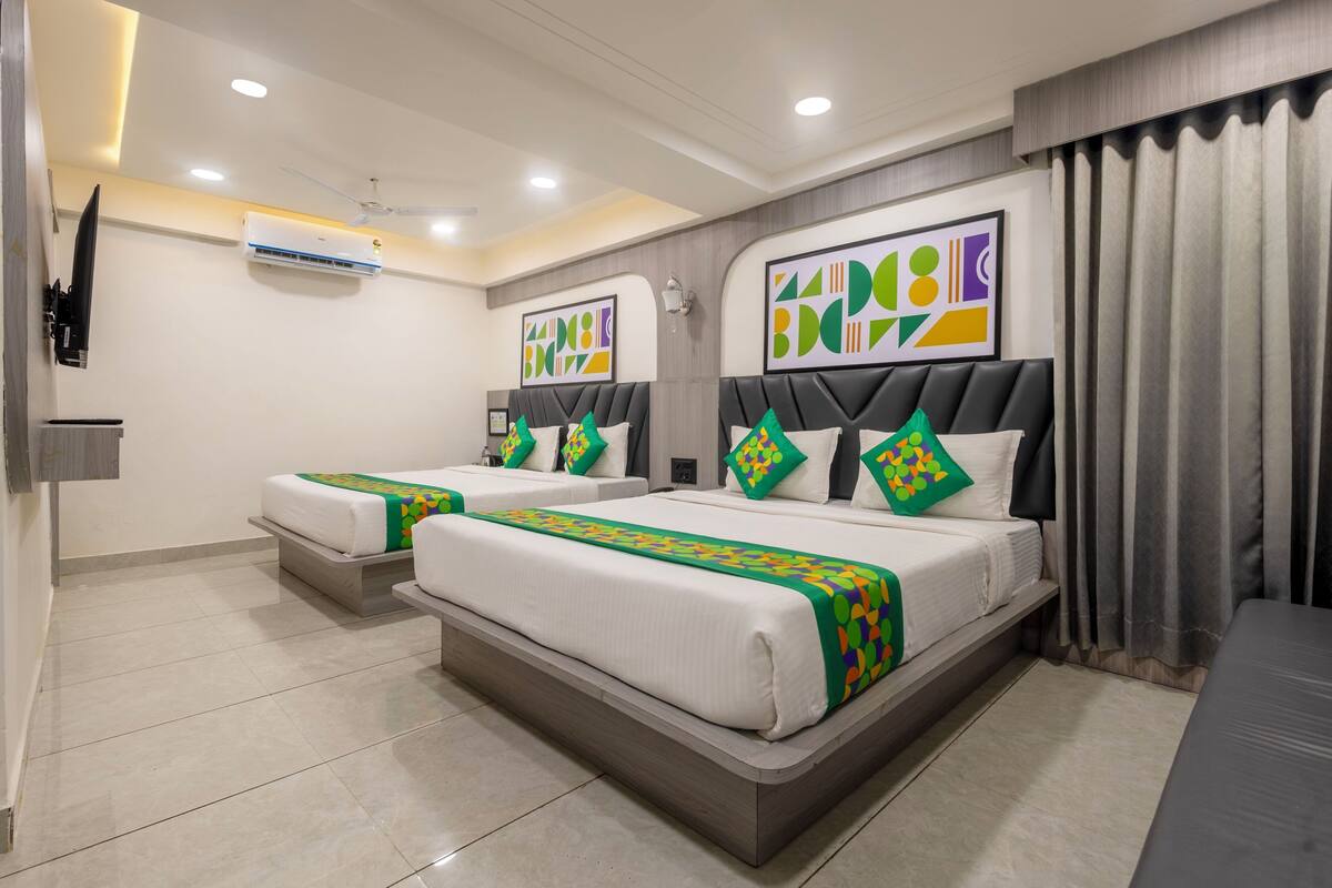 A hotel room with two beds, each with a headboard and pillows, a flat-screen TV mounted on the wall, and an air conditioning unit.