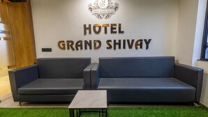 Ein Empfangsbereich mit einem Schild, auf dem 'HOTEL GRAND SHIVAY' steht, sowie zwei dunkel gefärbte Sofas und einem kleinen Tisch davor.