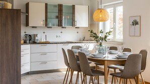 Une cuisine moderne avec des meubles blancs, une table à manger en bois et des chaises. Un luminaire est suspendu au-dessus de la table.