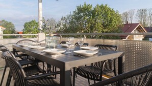 Un espace de restauration en plein air avec une table dressée pour quatre personnes, entourée de chaises en osier, et un récipient en verre contenant des plantes vertes.