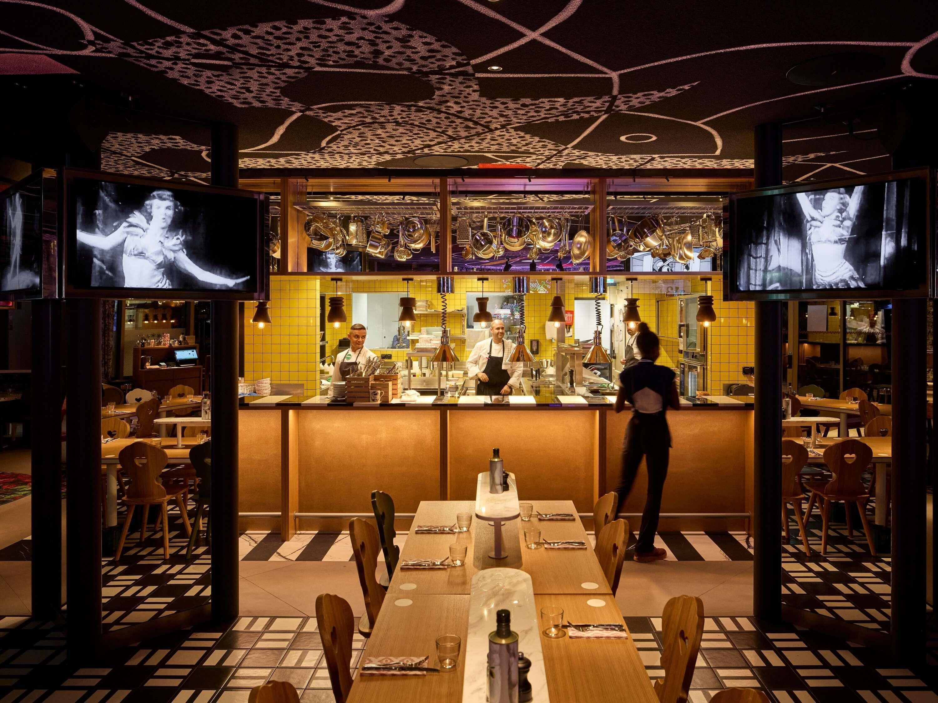 Un restaurante con zona de bar, varias mesas y suelo estampado.