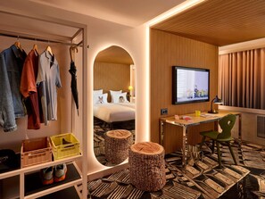 A hotel room with a bed, a TV, a desk, and a clothing rack. - Mama Shelter Zurich (Zurich)