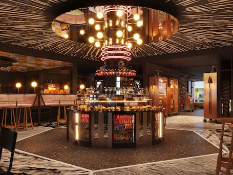 A bar area with a circular bar counter, stools, and a ceiling light fixture.. Mama Shelter Zurich