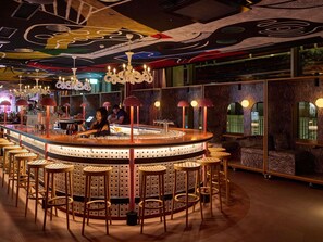 Un espace bar doté d’un comptoir circulaire, de nombreux tabourets et d’un plafond orné de motifs abstraits.