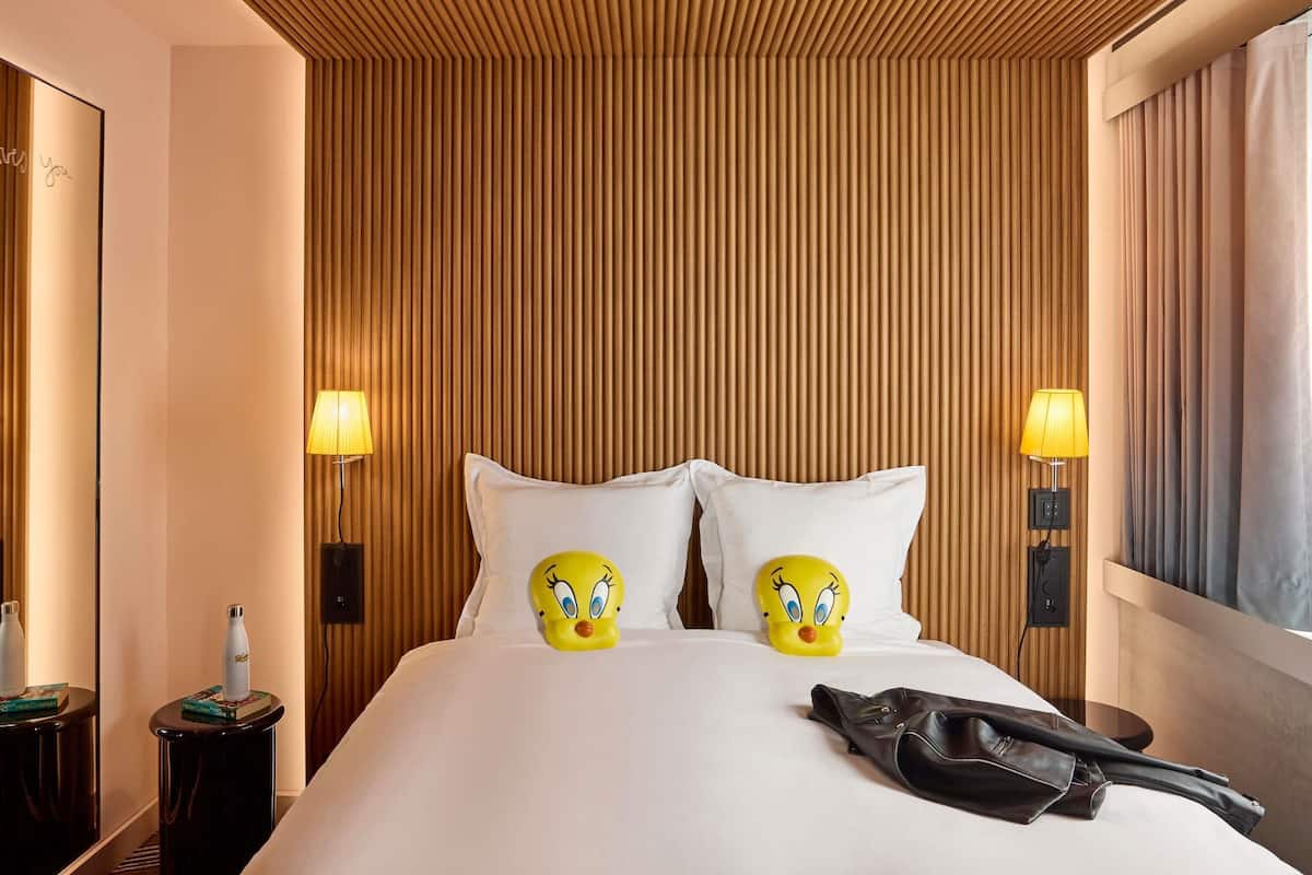 Camera d'albergo con testiera in legno a listelli, due lampade, un letto con biancheria bianca e due cuscini a forma di personaggi dei cartoni animati.
