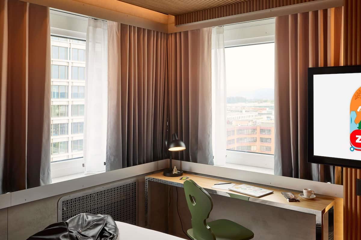 Una camera d'albergo con una scrivania, una sedia e un'ampia finestra con tende.
