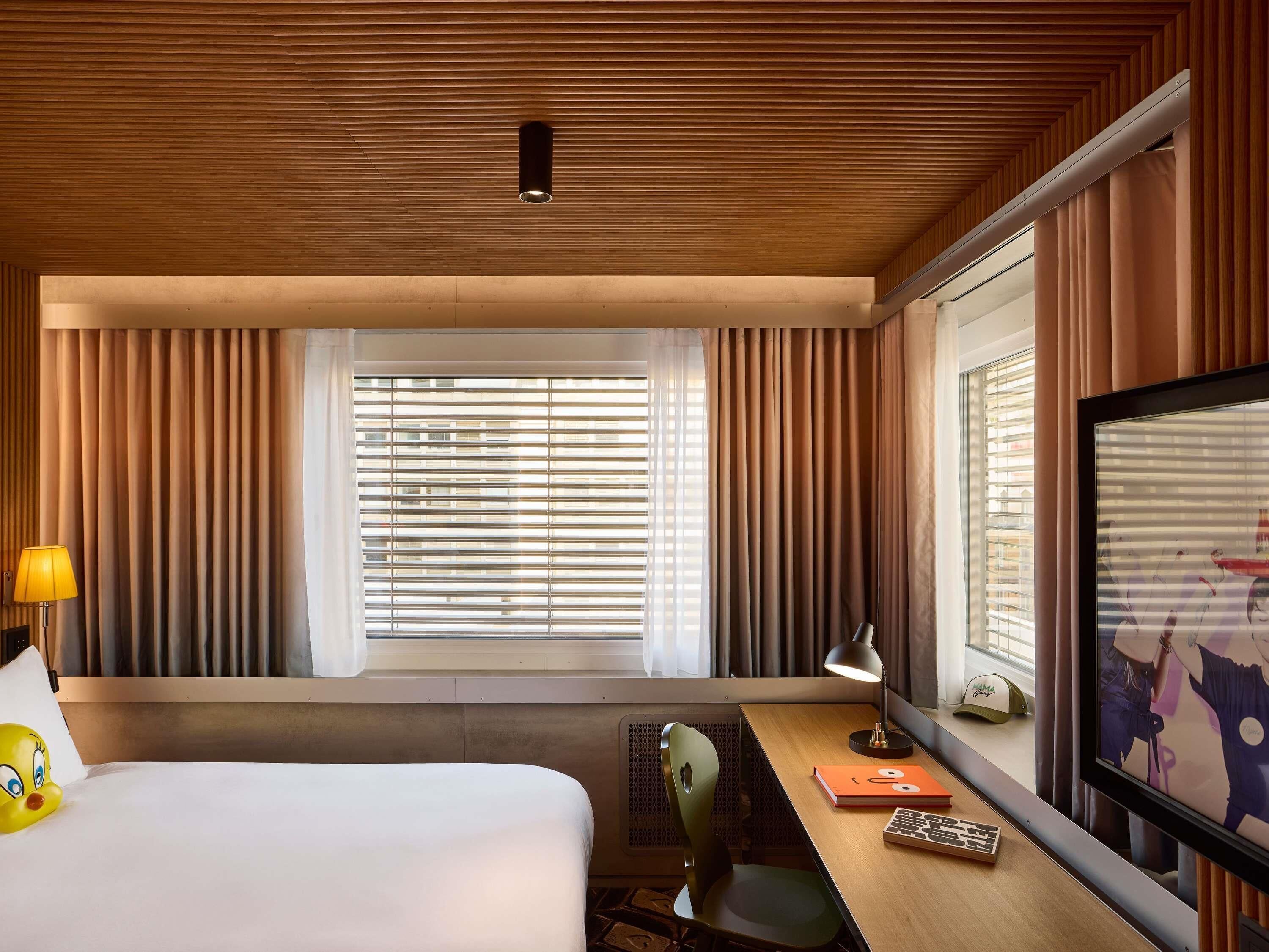 A hotel room with a bed, desk, chair, lamp, and a television.