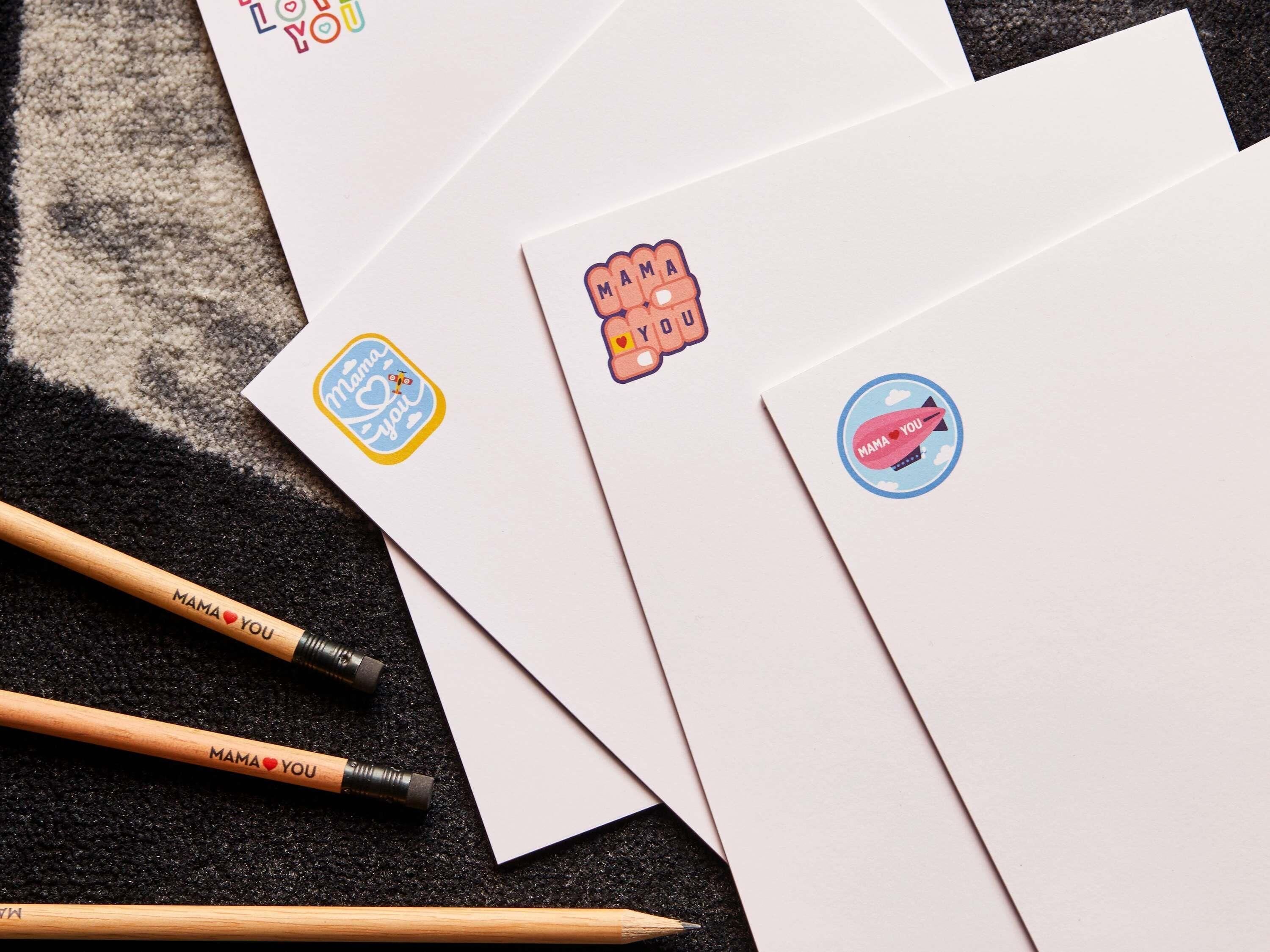 Four envelopes with 'MAMA YOU' stickers, two pencils, and a textured surface.