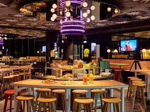 Un restaurant moderne doté d’un bar central, de plusieurs espaces pour s’asseoir et d’une variété de présentoirs pour les plats et les boissons.