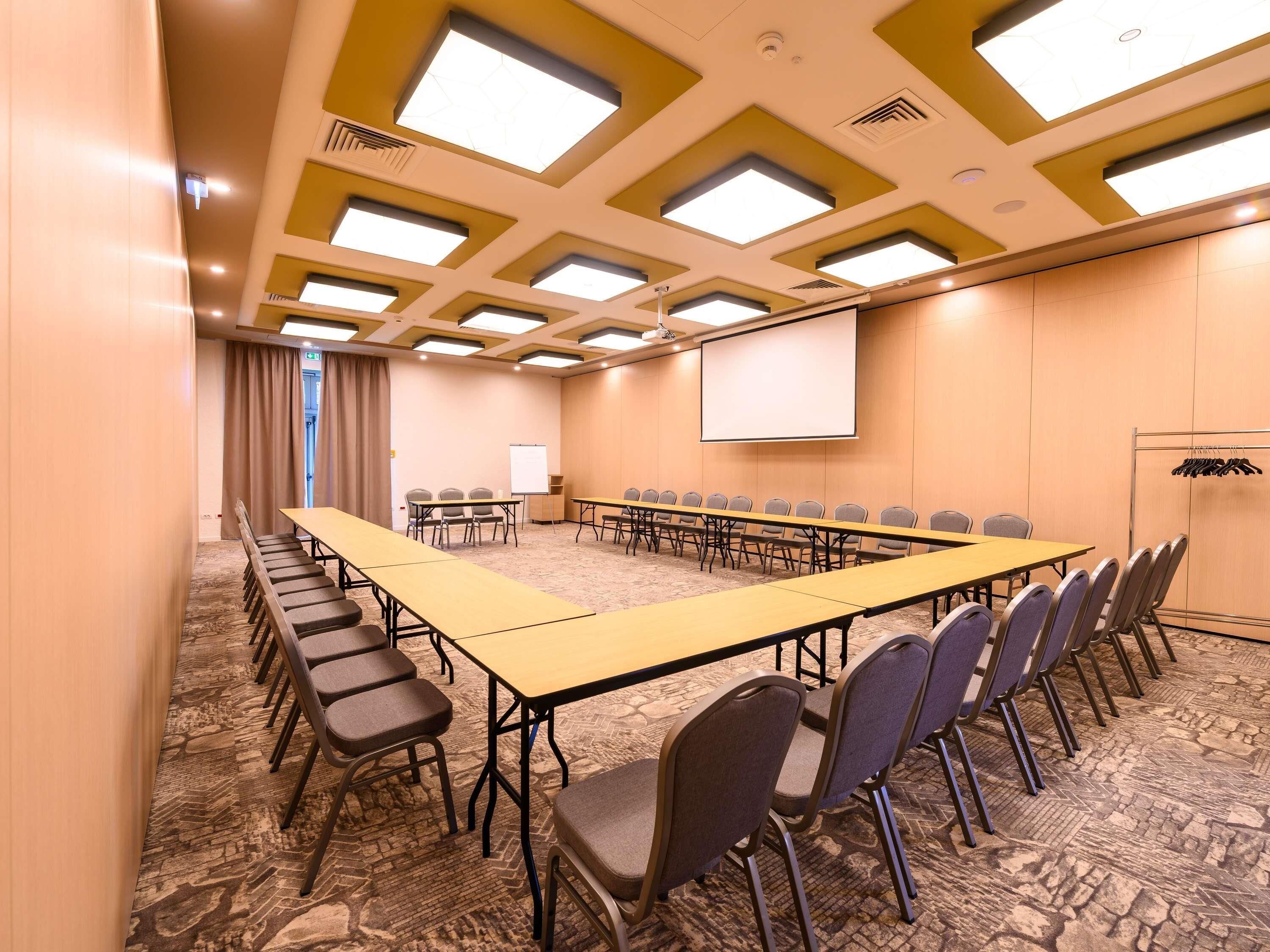 Uma sala de conferências com uma mesa comprida, cadeiras, uma tela de projetor e piso coberto de carpete.