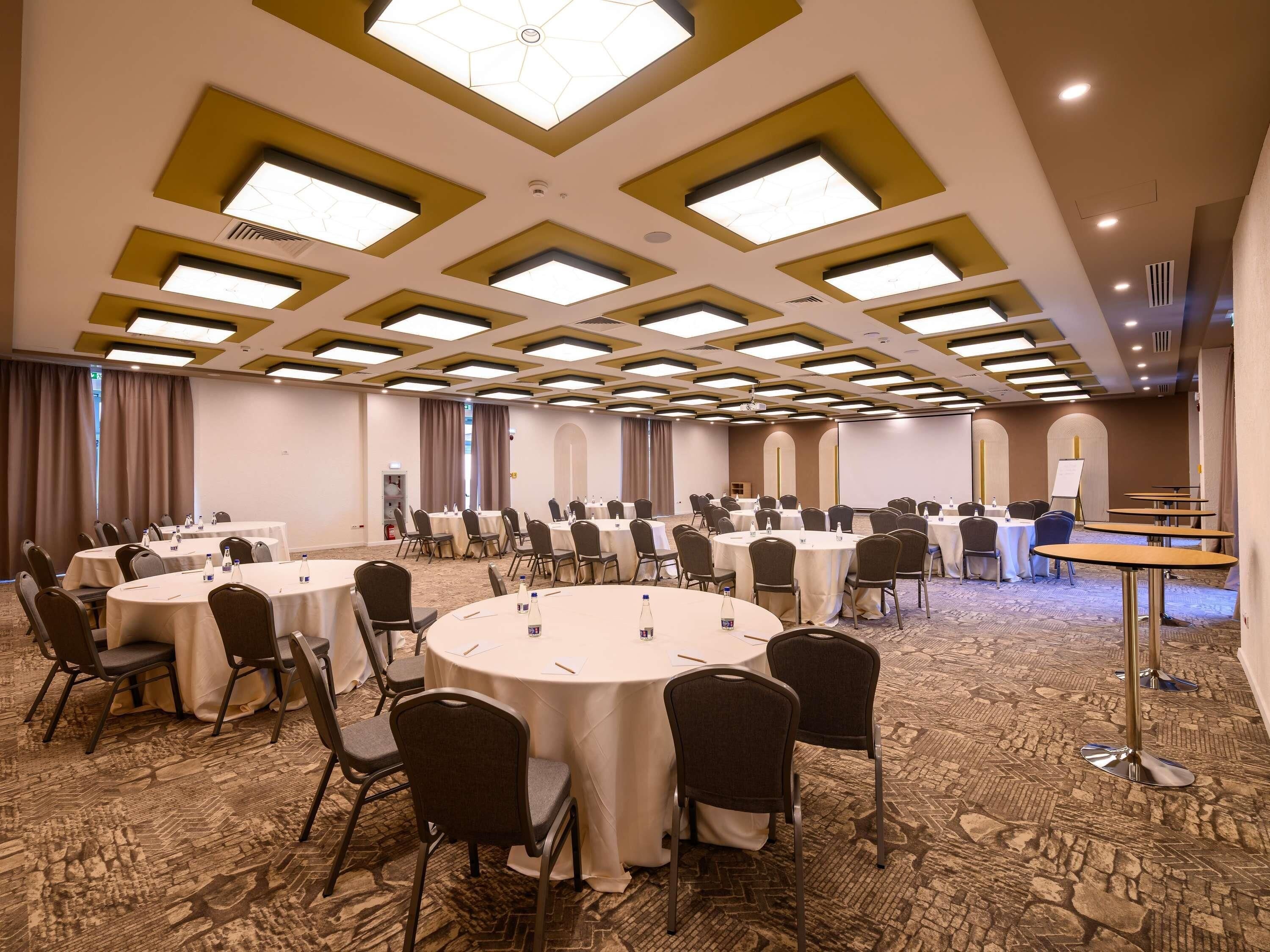 A conference room with multiple round tables, chairs, and a projector screen.