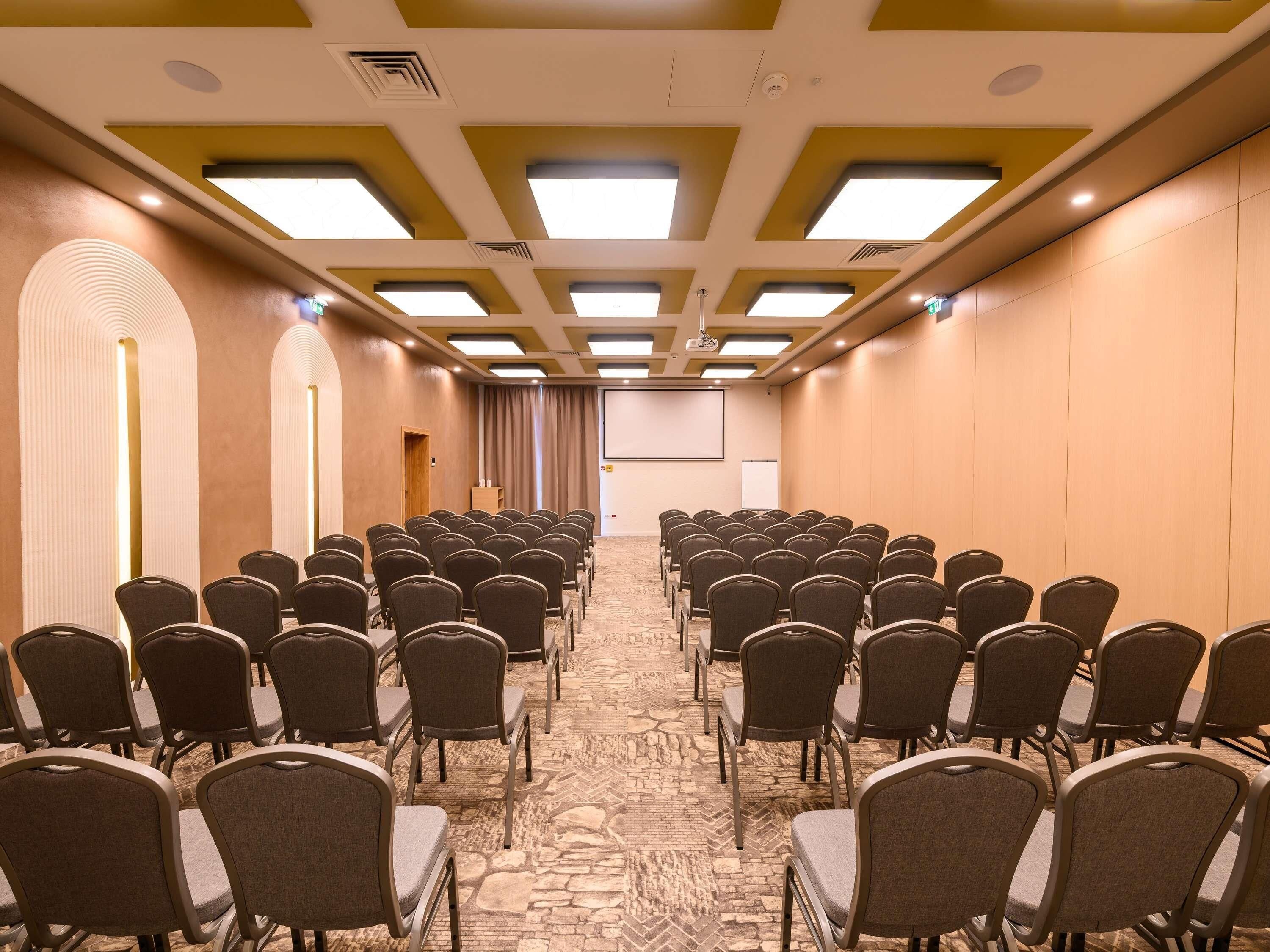 A conference room with rows of chairs, a projector screen, and a carpeted floor.