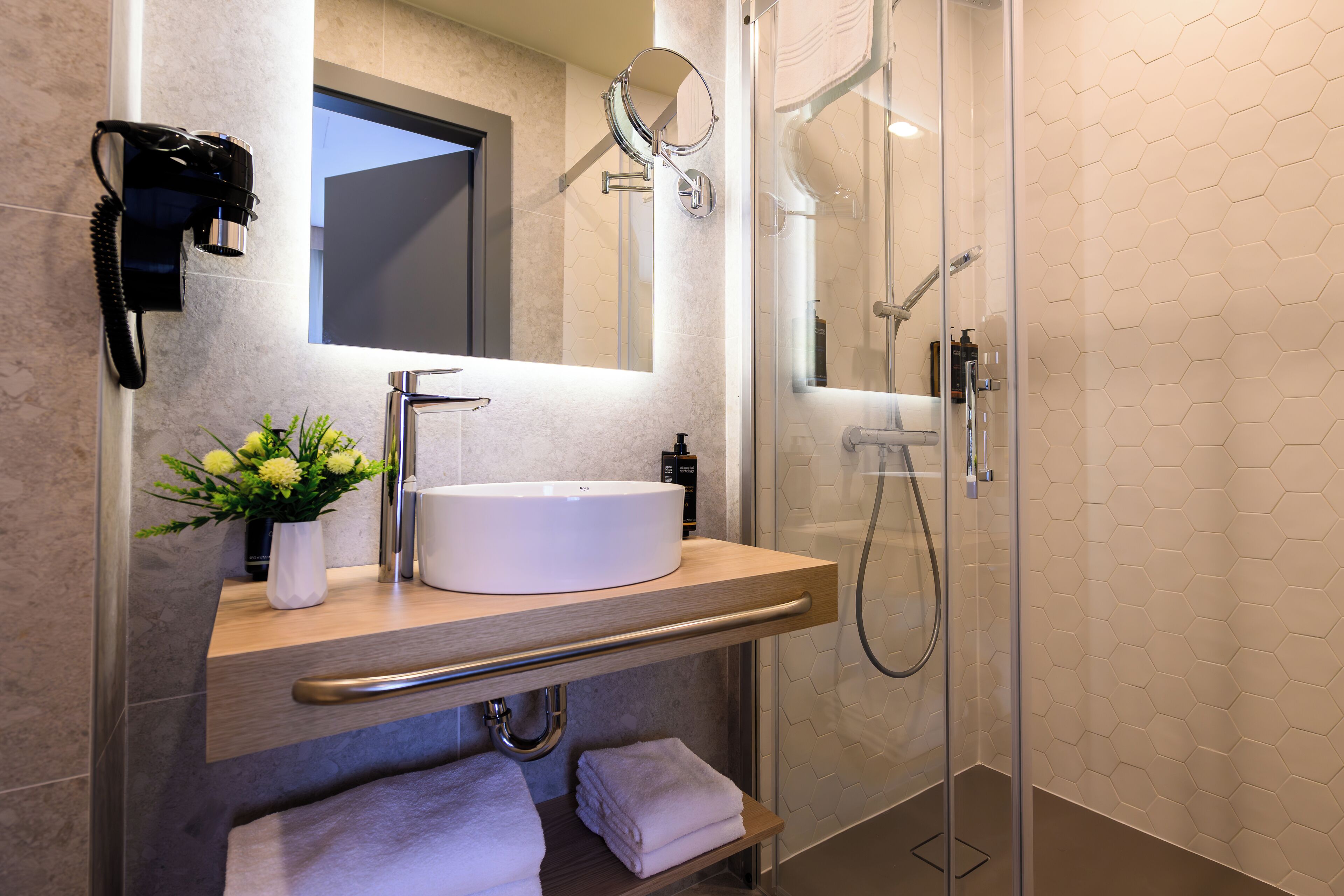 A modern bathroom with a white sink, a handheld mirror, and a glass-enclosed shower.