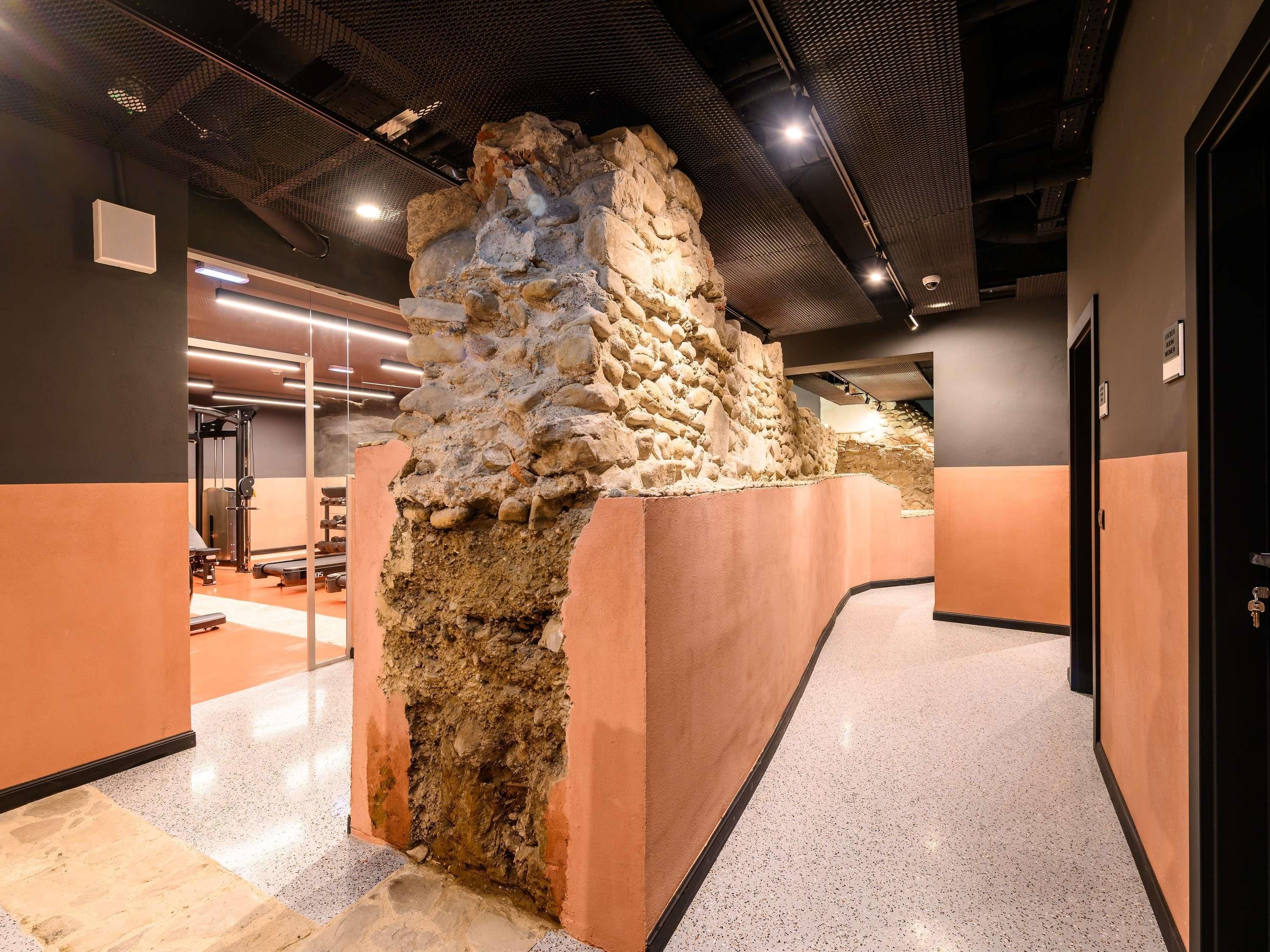 A hallway with a central stone structure, a door on the right, and a bench on the left.