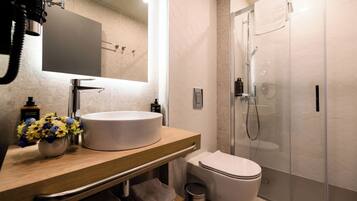 Un bany modern amb un lavabo rodó, un vàter i una dutxa amb envàs de vidre.